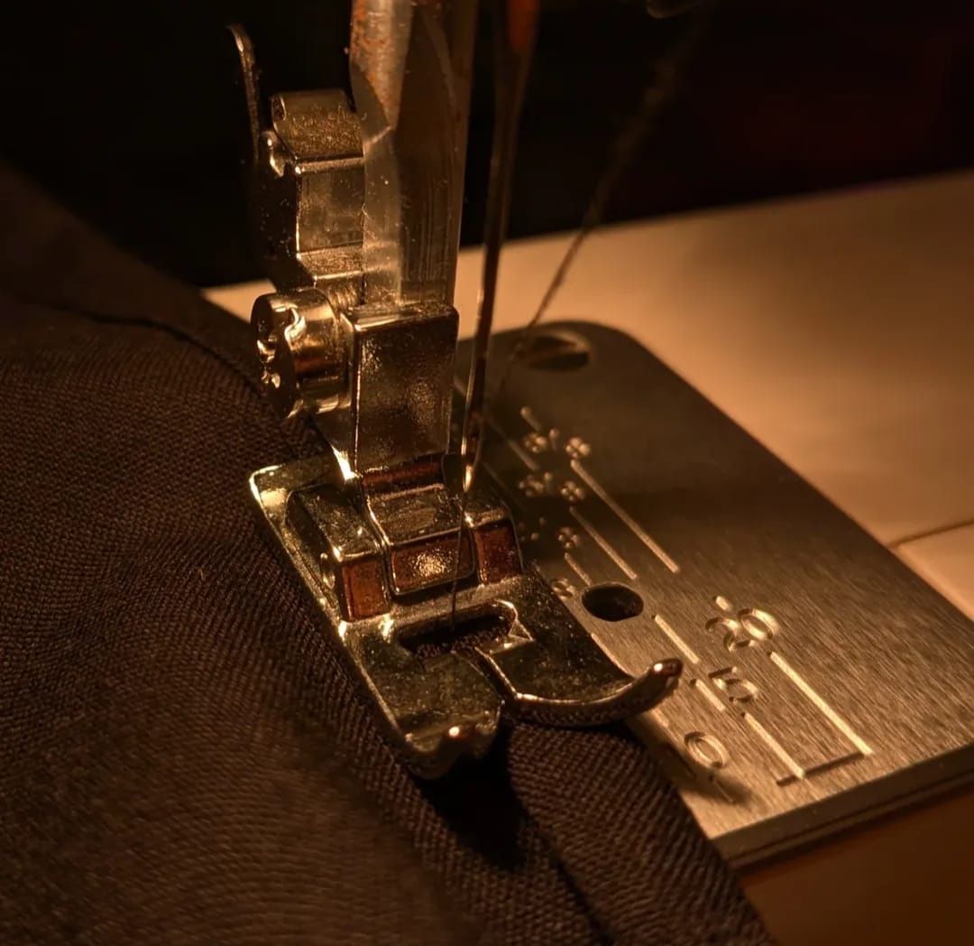 Close-up of a sewing machine stitching dark fabric under warm light